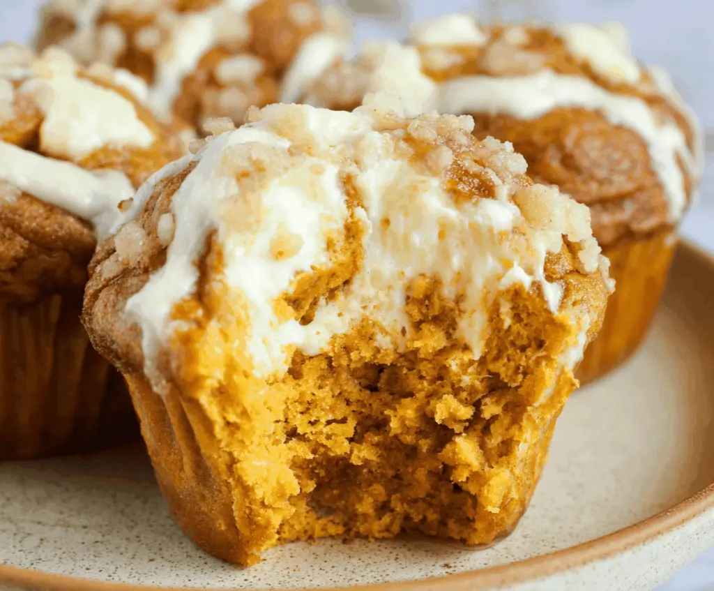 Freshly baked pumpkin cream cheese muffins with a golden crust and creamy filling on a rustic wooden table.