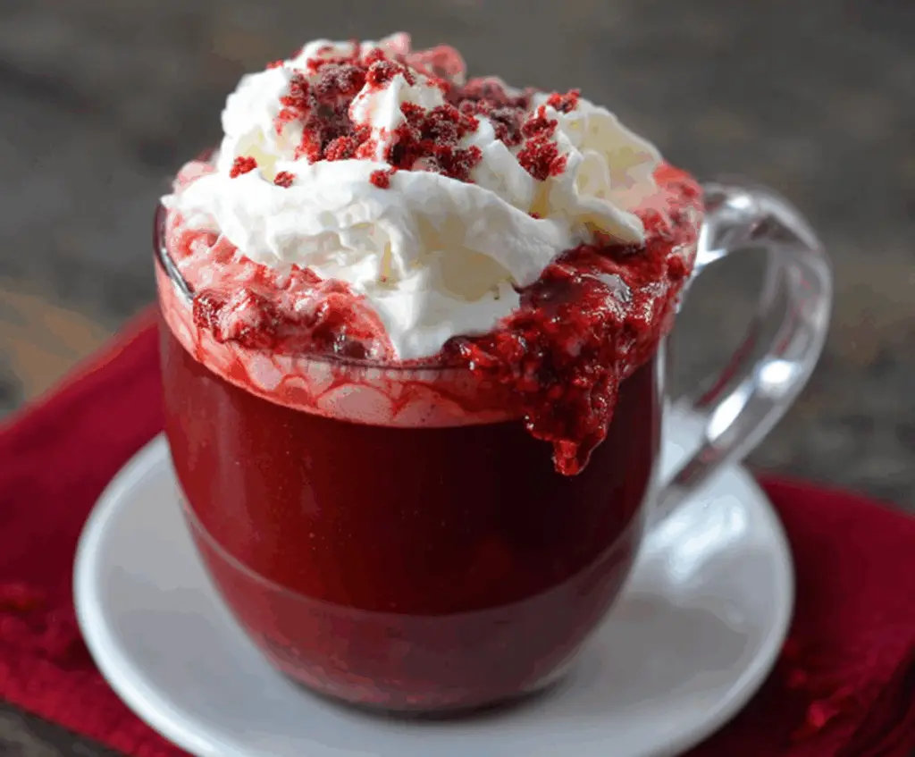 A steaming cup of Red Velvet Hot Chocolate topped with whipped cream and red sprinkles, perfect for cold evenings.