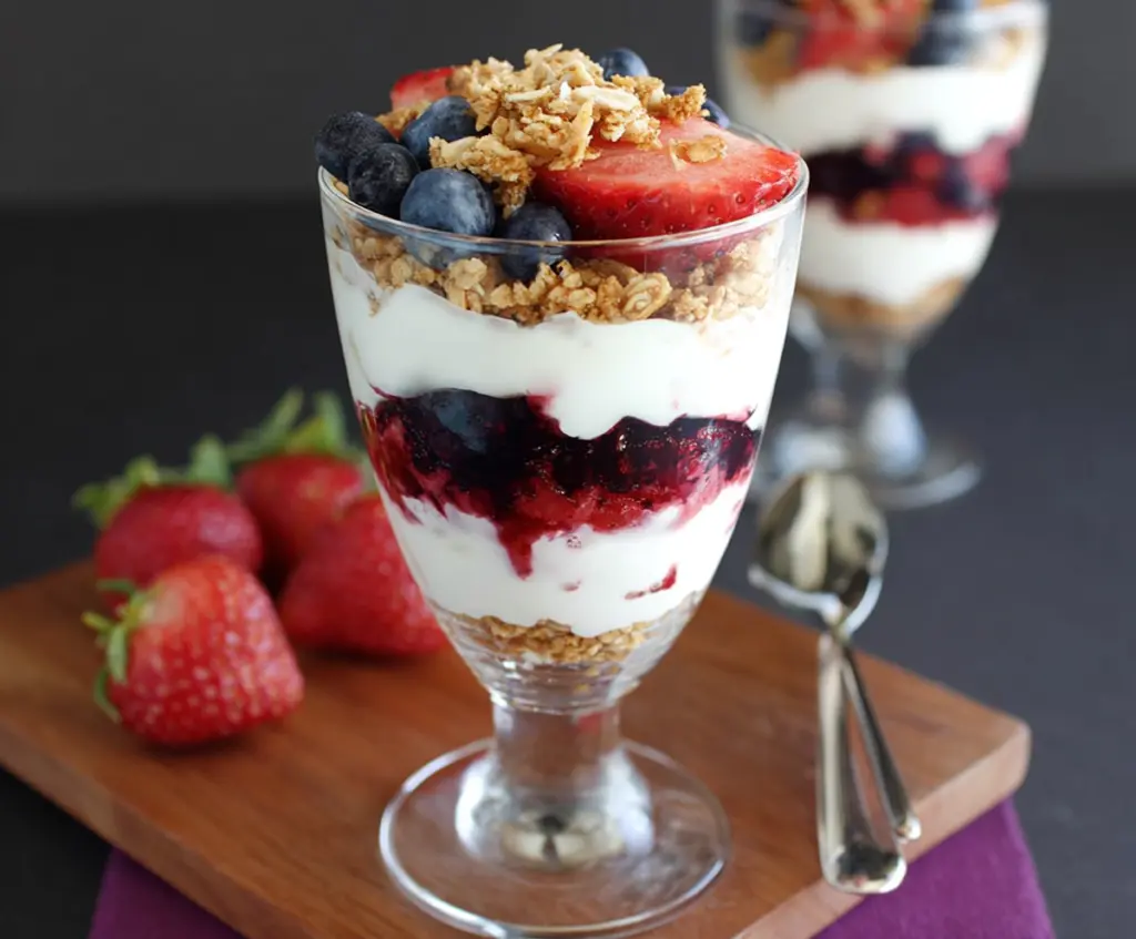 Delicious Greek Yogurt Berry Parfaits with fresh strawberries blueberries and granola in a glass bowl.